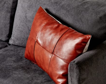 Stylish handcrafted cushion featuring glossy brown leather patchwork top creating striking contrast to charcoal grey colored sofa, perfect for minimalist interior decor