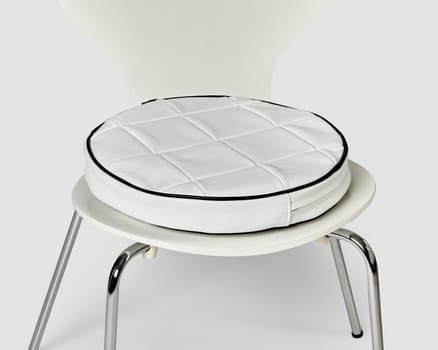 Modern handcrafted round white leather patchwork seat cushion with elegant black piping, resting on classic chrome-legged chair. Stylish accessories for interior design