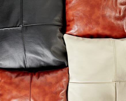 Closeup of view of handcrafted sofa cushions made from smooth genuine black, brown and cream leather with neat decorative stitching. Stylish soft interior accessories. Natural textured background