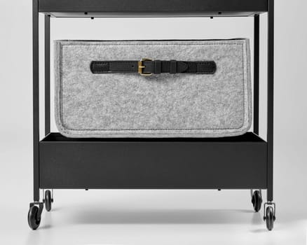Stylish grey felt drawer decorated with applied black leather handle placed on shelf in metal office trolley. Craft accessories for interior design, stationery and document storage