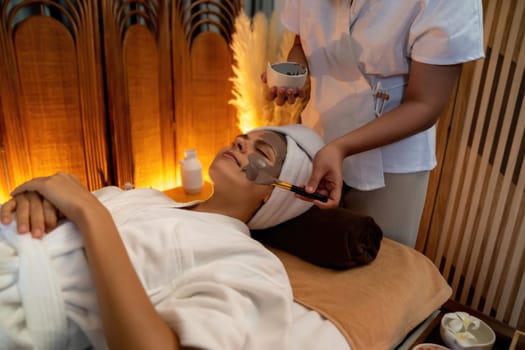 Serene ambiance of spa salon, woman customer indulges in rejuvenating with charcoal face cream massage with warm lighting candle. Facial skin treatment and beauty care concept. Quiescent