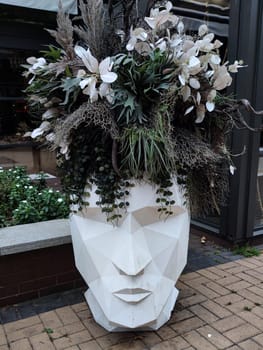 outdoor planter in the shape of a human head with flowers instead of hair close-up