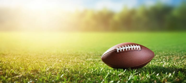 Close-up of an American football on green grass with sunlight in the background, suggesting a game or practice session.