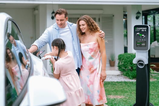 Happy little young girl learn about eco-friendly and energy sustainability as she help her family recharge electric vehicle from home EV charging station. EV car and modern family concept. Synchronos