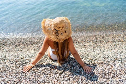 Beach Relaxation woman in hat sits on a pebble beach enjoying the sunshine. The concept of travel, vacation at sea.