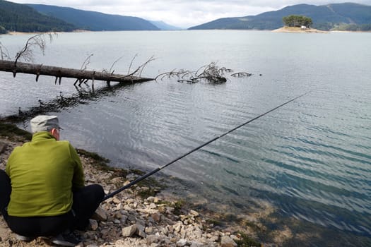 man fishing on the shore of a mountain lake.