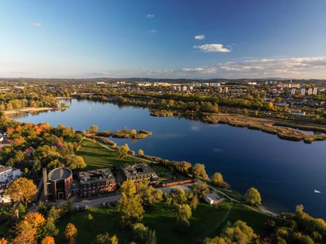 Aerial view of Bagry lake and autumn forest in Poland. Amazing panoramic landscape with waters of spectacular Bagry lagoon and road along beach, houses of town and scenic tops of trees under blue sky