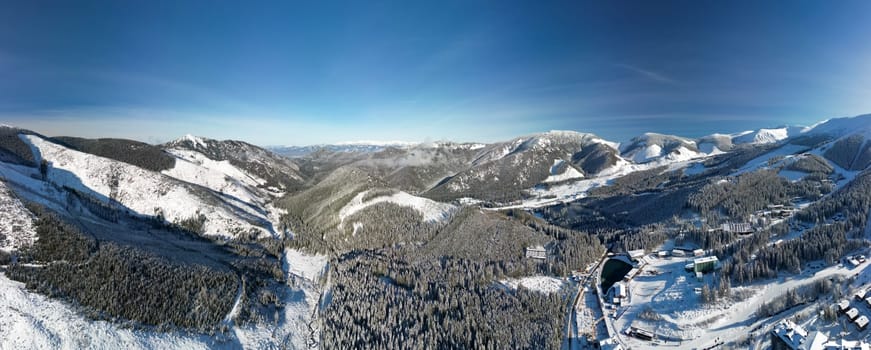 Aerial winter view of Demanovska Dolina village in Low Tatras mountains, Slovakia. Drone panoramic view to countryside landscape, high peaks and tops of frozen fir trees, houses and road of town