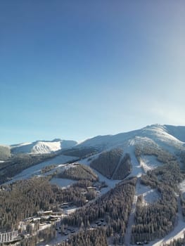 Aerial winter view of snowy cable car station and ski resort houses of Demanovska Dolina village. Drone view over pine trees tops and hotels on rocks in evening Low Tatras mountains, Slovakia