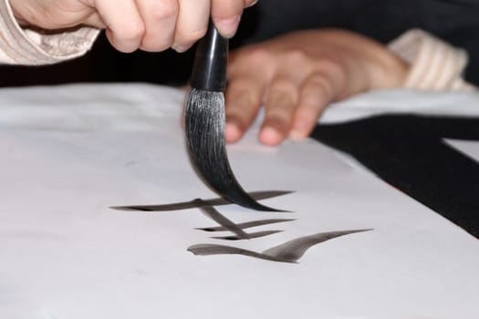 Brush drawing a hieroglyph with black ink on white rice paper close-up