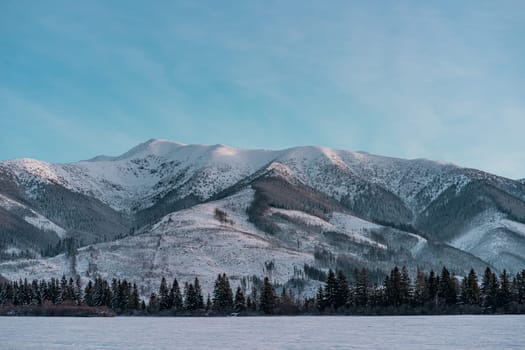 Winter mountain landscape, sun rays on slopes and pine forest at foot of cliffs of Low Tatras, Slovakia