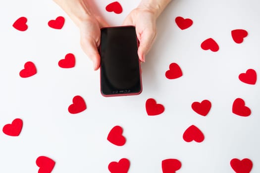 Hands holding a smartphone with scattered red hearts on a white background. Mockup, place for inscription