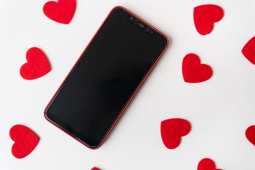 Smartphone surrounded by red felt hearts on a white background. Place for an inscription