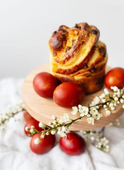 Delicious pastries on a wooden board surrounded by ripe red eggs and delicate white flowers. Easter holiday concept