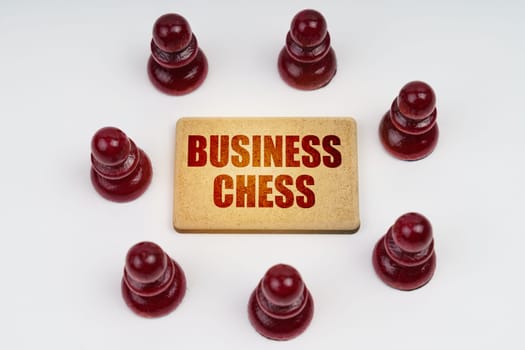 Business concept. On a white background, pawns stand around a sign with the inscription - Business Chess