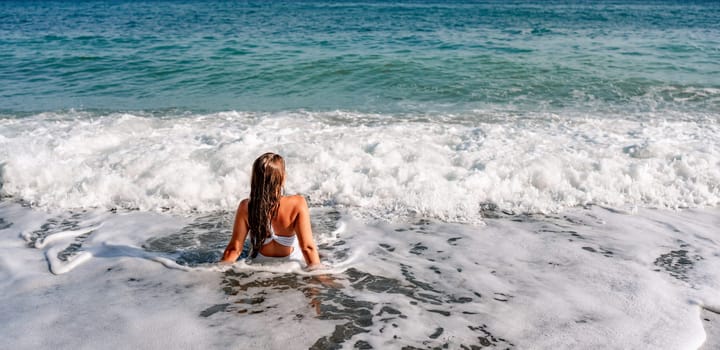 Happy woman in bikini sits on the sea beach. Tanned girl sunbathing on a beautiful shore. Summer vacation or holiday travel concept.