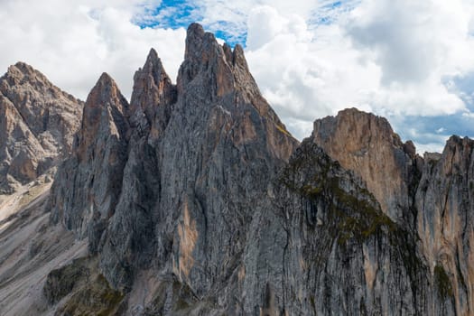 Rocky shady peak of Seceda mountain range against cloudy sky. Summit of long ridgeline in touristic Italian Alps on summer day aerial view