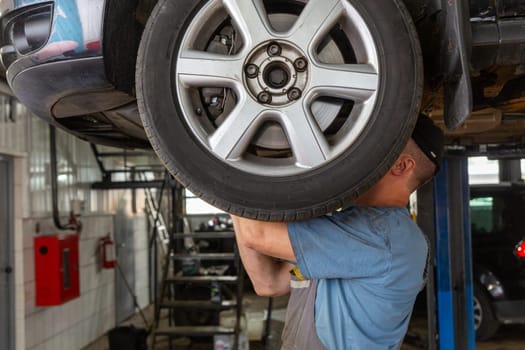 Car mechanic working in auto repair shop. Man in uniform working with car engine.