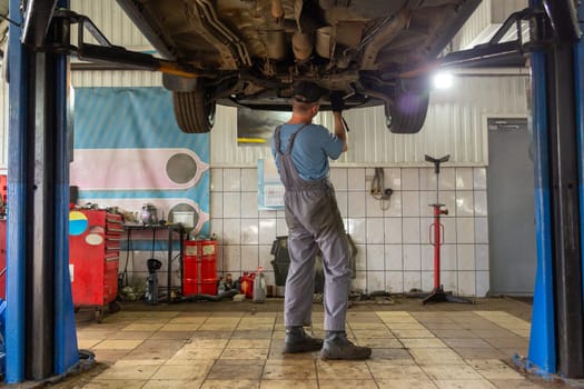 Car mechanic working in auto repair shop. Man in uniform working with car engine.