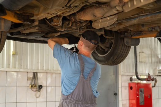 Car mechanic working in auto repair shop. Man in uniform working with car engine.