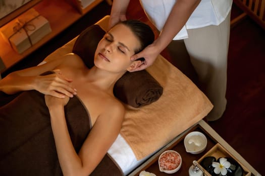 Caucasian woman enjoying relaxing anti-stress head massage and pampering facial beauty skin recreation leisure in warm candle lighting ambient salon spa in luxury resort or hotel. Quiescent