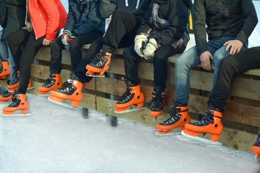 Teenagers in orange skate on the ice.