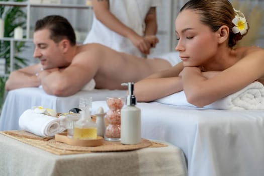 Caucasian couple customer enjoying relaxing anti-stress spa massage and pampering with beauty skin recreation leisure in day light ambient salon spa at luxury resort or hotel. Quiescent
