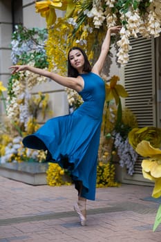 Beautiful Asian ballerina dances against the background of a building decorated with flowers. Vertical photo
