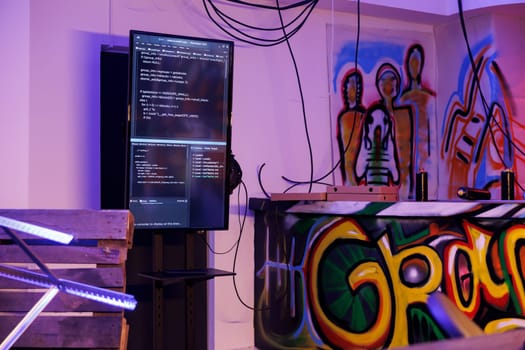 Malware running code for database hacking on screen in abandoned warehouse. Malicious software programming and password cracking on vertical display in dark room with graffiti