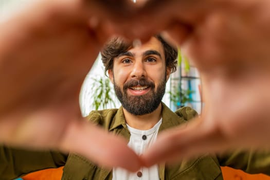 I love you. Happy middle eastern man at home living room couch makes symbol of love showing heart sign to camera express romantic feelings express sincere positive feelings. Charity gratitude donation