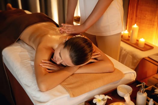 Caucasian woman customer enjoying relaxing anti-stress spa massage and pampering with beauty skin recreation leisure in warm candle lighting ambient salon spa at luxury resort or hotel. Quiescent