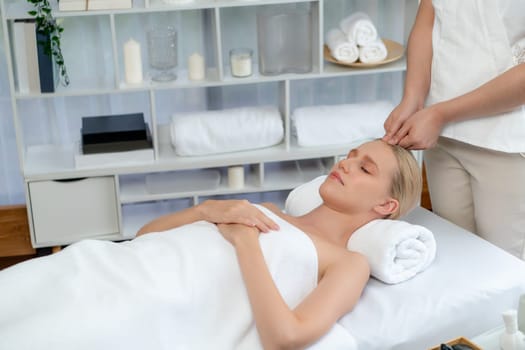 Caucasian woman enjoying relaxing anti-stress head massage and pampering facial beauty skin recreation leisure in dayspa modern light ambient at luxury resort or hotel spa salon. Quiescent