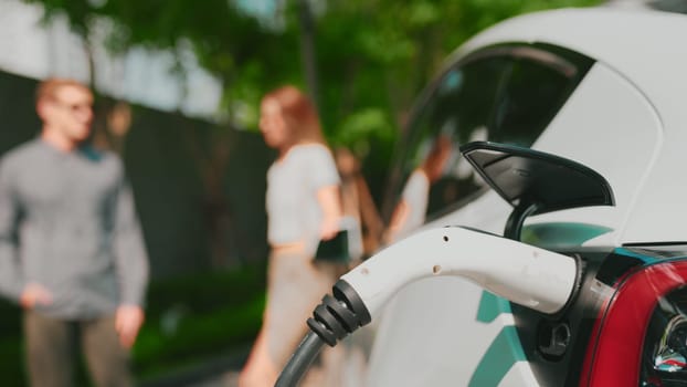 Focused EV electric car charging in green sustainable city outdoor garden in summer show lifestyle on blur background of young couple in urban green sustainable rechargeable electric vehicle innards