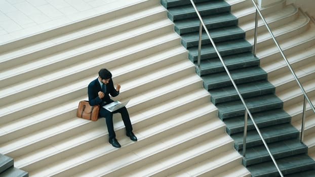 Top view business man celebrate successful project while sitting at stairs. Smart project manager getting new gob, getting promotion, increasing sales while calling friends by using laptop. Exultant.