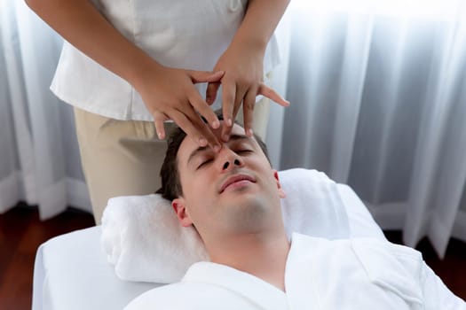 Caucasian man enjoying relaxing anti-stress head massage and pampering facial beauty skin recreation leisure in dayspa modern light ambient at luxury resort or hotel spa salon. Quiescent