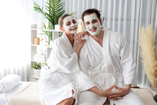 Blissful couple in bathrobe with facial cream mask enjoying serene ambiance of spa salon resort or hotel during holiday. Pampering face spa and skincare treatment with essence relaxation. Quiescent