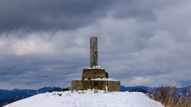 Stone concrete marker on summit of snowy mountain on cloudy day. High quality photo