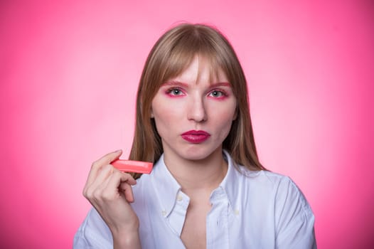 Portrait of a young woman with braces and bright makeup chewing gum on a pink background