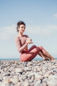 Young woman with long hair in white swimsuit and boho style braclets practicing outdoors on yoga mat by the sea on a sunset. Women's yoga fitness routine. Healthy lifestyle, harmony and meditation