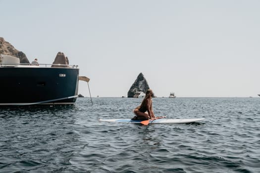 Close up shot of beautiful young caucasian woman with black hair and freckles looking at camera and smiling. Cute woman portrait in a pink bikini posing on a volcanic rock high above the sea