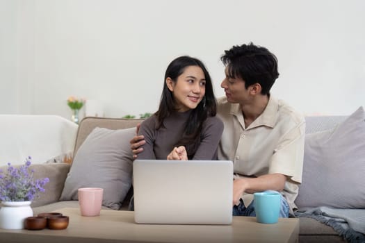 Young couple asian using laptop together while sitting on sofa at home.