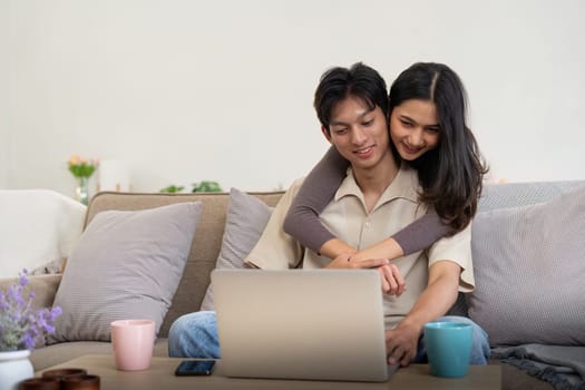 Young couple asian using laptop together while sitting on sofa at home.