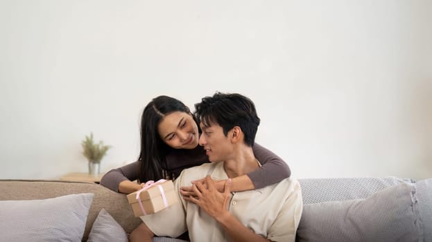 Romantic young asian couple embracing giving present in living room at home. Fall in love. Valentine concept. Surprise gift.