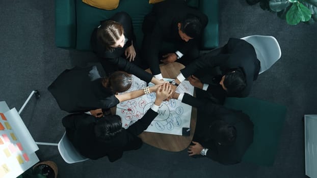 Top view of professional business people putting hand together to celebrate successful project while using mind map to brainstorm idea. Happy startup diverse team stacking hands together. Directorate.