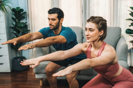 Athletic and sporty couple doing squat together during home body workout exercise session for fit physique and healthy sport lifestyle at home. Gaiety home exercise workout training concept.