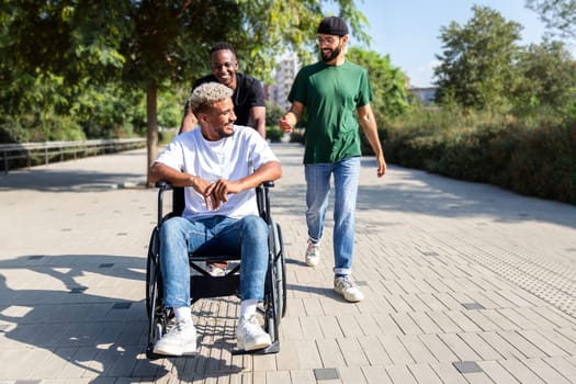 Young disabled Black man in a wheelchair and his male friends walking together in the city. Friendship concept.