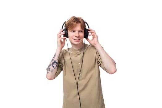young red-haired man with glasses dressed in a brown shirt with wired large headphones.