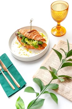 Croissant sandwich with ham, cheese and vegetables in white plate. Top view with copy space on white table