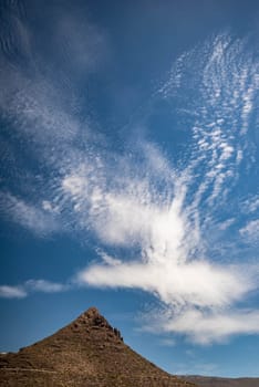 Summer landscape wallpaper with a mountain on blue sky background with beautiful white clouds. Vertical photo of a rocky mountain with green shrubs on sunny day. Concept of hiking. Nature of Tenerife