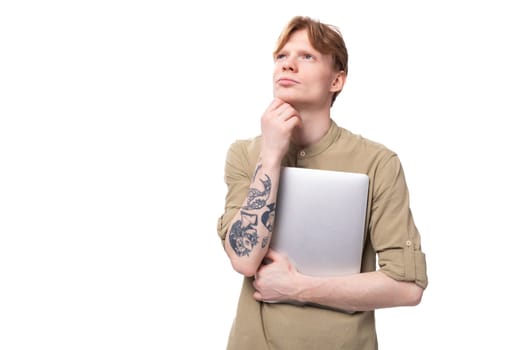 young handsome red-haired man in glasses and a shirt holds a laptop for remote work.